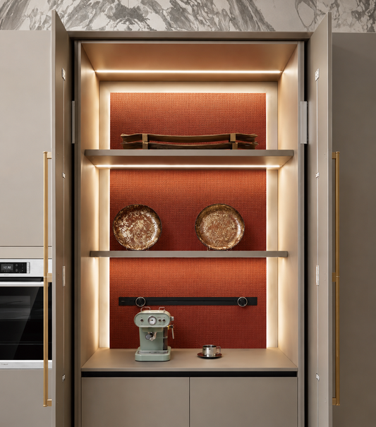 A modern built-in cabinet display area with open doors, warm LED lighting, a terracotta-orange textured back panel, two floating shelves, decorative plates, and a countertop appliance on a beige cabinet base.