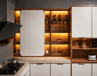 A modern kitchen cabinetry and bar shelving unit with white doors, warm wood trim, and built-in under-cabinet lighting. The shelves display glassware, bottles, and small accessories, set against a dark gray wall.