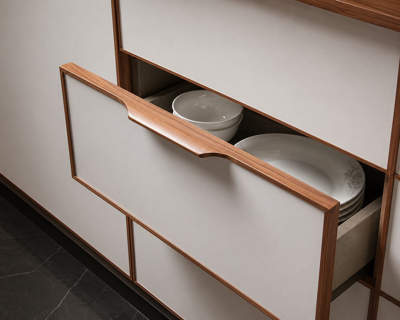 A close-up of a modern kitchen cabinet drawer with a light wood handle, partially open to reveal white ceramic bowls and plates inside.