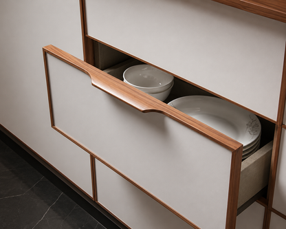 A close-up of a modern kitchen cabinet drawer with a light wood handle, partially open to reveal white ceramic bowls and plates inside.