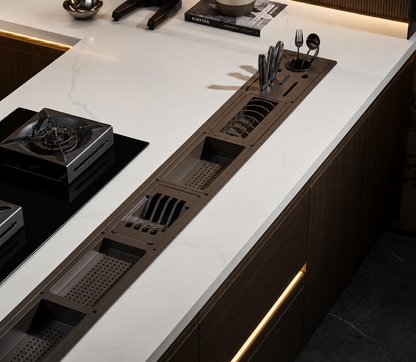 A modern kitchen island with a white marble countertop and dark wood cabinetry, featuring a long recessed slot with integrated dish rack, utensil holder, and storage compartments.