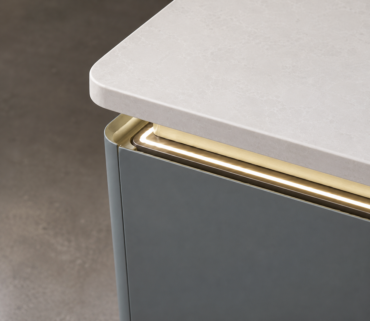 Close-up of a modern kitchen cabinet corner with a light gray stone-look countertop, a dark gray front, and a brushed gold metal trim accent.