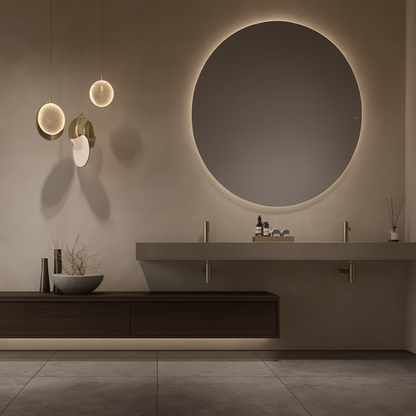 Floating double-surface vanity with warm wood cabinetry, extended stone countertop, gold fixtures, circular backlit mirror, and sculptural pendant lighting – SAIBA Homes.