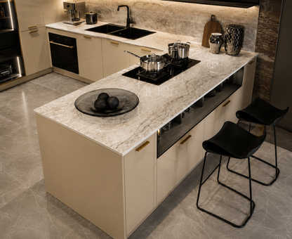 A modern kitchen island with a white marble-look countertop, cream cabinetry, a built-in black cooktop, two black bar stools, and a black bowl of fruit on a tiled kitchen floor.
