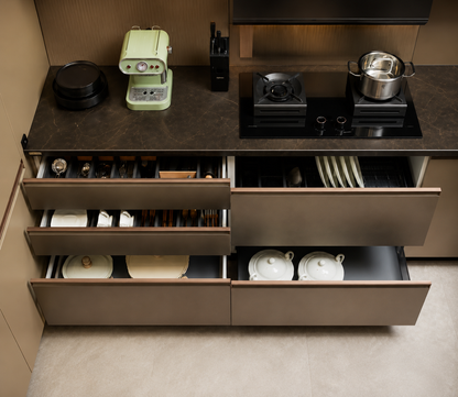 A top-down view of a modern kitchen cabinet system with dark countertops, open drawers showing white dishes and cutlery, and a black built-in gas cooktop with a stainless steel pot.