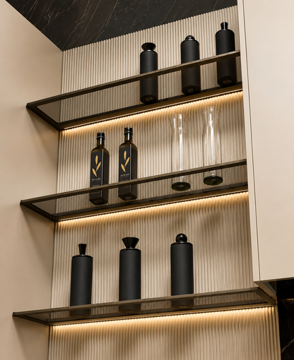Modern glass shelves with dark metal frames displaying matte black bottles and clear glass vessels against a beige ribbed wall with warm under-shelf lighting.
