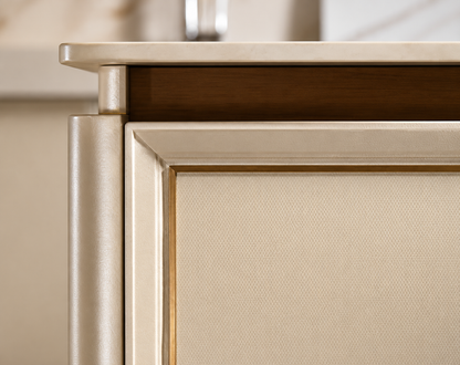 Close-up detail of a modern cabinet or sideboard corner, showing a brushed gold metal frame, a textured beige fabric front panel, and a dark wood shelf above.
