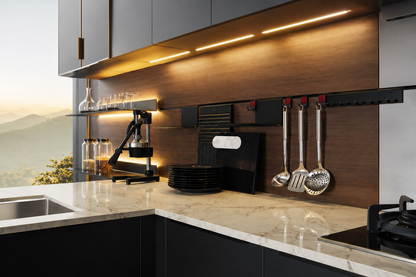 Modern kitchen interior with dark cabinetry, a light marble countertop, a wood-look backsplash, under-cabinet LED lighting, and hanging kitchen utensils.
