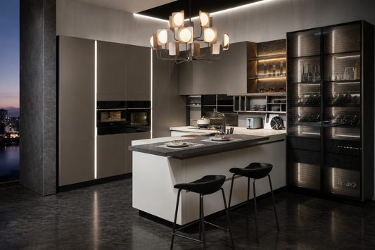A luxury modern kitchen interior featuring a central white island with a dark countertop, two black bar stools, sleek dark cabinetry with vertical LED light strips, glass-front wine storage, and a multi-light chandelier overhead.