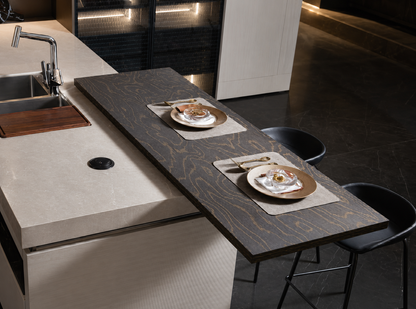 A modern kitchen island with a dark wood-look extension table, set with two place settings and two black bar stools in a dark, contemporary kitchen.