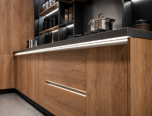 Modern kitchen cabinetry with warm wood grain doors, a dark countertop, and integrated under-cabinet lighting. Stainless steel pots are visible on the cooktop, and open shelving with built-in LED lighting stands in the background.
