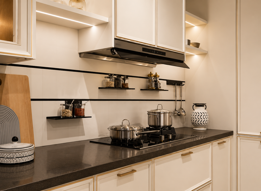 A modern kitchen interior with cream cabinets, a dark countertop, built-in black floating shelves, a stainless steel range hood, and cookware including two pots and a patterned ceramic container.