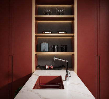 A modern kitchen setup featuring a white marble countertop with a red rectangular sink, a chrome faucet, and a built-in wooden shelving unit with warm lighting and dark red side cabinets.