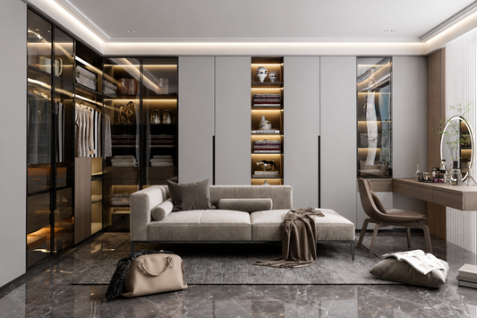 A modern, luxurious home office and dressing room setup featuring a light beige sofa, a vanity desk with a round mirror, and extensive built-in walk-in closets with glass doors and warm LED lighting, all set on a dark marble floor.