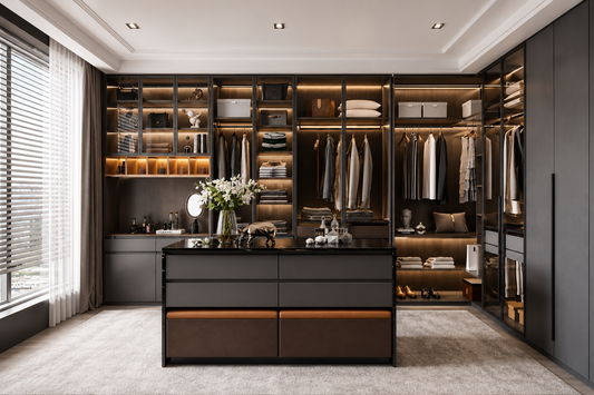 A luxury walk-in closet room featuring a large black central island with drawers, extensive built-in shelving and hangers filled with clothing, warm under-cabinet lighting, and a light gray carpet.